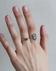Hand wearing a gold ring with a green gemstone on a neutral background