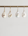 Four pearl earrings hanging on a rod against a light gray background