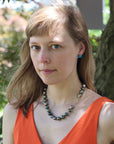 Woman wearing an orange top and a necklace with a blurred natural background