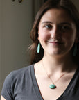 Woman wearing a necklace with a green pendant against a neutral background