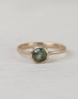 Gold ring with a green gemstone on a light gray background