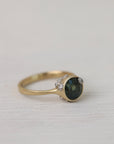 Gold ring with a dark gemstone and small barnacles on a light fabric background