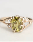 Gold ring with a green gemstone and small diamonds on a light gray background
