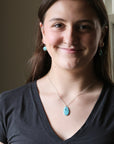 Woman wearing a necklace with a blue pendant indoors