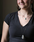 Woman wearing a black top and a necklace with a pendant indoors.