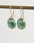 Green gemstone earrings on a thin rod against a light gray background
