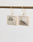 Pair of earrings with ship and whale design on a white background