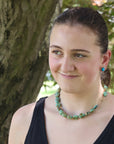 Woman wearing a green beaded necklace outdoors with trees in the background