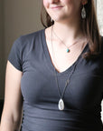Woman wearing a dark gray shirt with necklaces and earrings indoors.