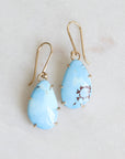 Pair of blue teardrop earrings on a gold earring stand against a light gray background