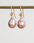 Pair of pink pearl earrings on a gold hook against a light gray background