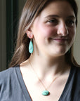 Woman wearing turquoise earrings and a necklace with a neutral background