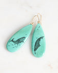 Teal earrings with whale design on a white background