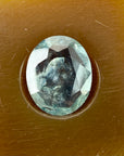 Greenish-blue oval gemstone in a brown setting on a textured brown background