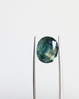 Green sapphire with inclusions held in tweezers