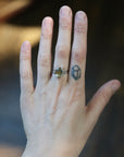 A close-up of a person's hand wearing a silver ring with a green gemstone, with a small geometric tattoo on one of the fingers.