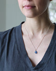 Person wearing a necklace with a blue pendant against a neutral background