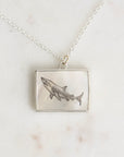 Silver necklace with a shark pendant on a marble surface