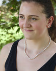 Woman wearing a pearl necklace and earrings outdoors with greenery in the background