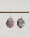 Pair of earrings with purple gemstones on a thin rod against a light gray background