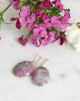 Earrings with pink and gray stones on a marble surface with flowers.