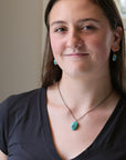 Woman wearing a black top and turquoise necklace and earrings indoors.