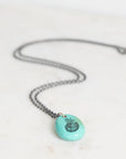 Necklace with a turquoise pendant featuring a black design on a light gray background