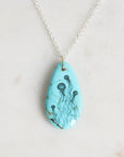 Turquoise pendant with jellyfish design on a silver chain against a light gray background