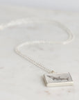 Silver necklace with a rectangular pendant featuring an engraved design on a light gray background