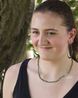 Woman wearing a black top and green necklace with trees in the background