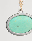 Necklace with a pendant featuring a green stone and gold accents on a light gray background