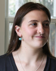 Woman wearing earrings and a necklace, standing indoors with a neutral background