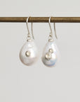 Pair of teardrop-shaped pearl earrings with silver hooks on a light gray background