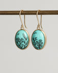 Pair of earrings with turquoise oval stones and gold accents on a gray background