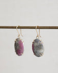 Pair of earrings with purple gemstones on a thin rod against a light gray background