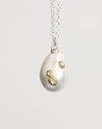 Pearl pendant with gold accents on a silver chain against a light gray background