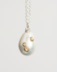 Pearl pendant with gold accents on a silver chain against a light gray background
