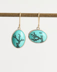 Pair of earrings with turquoise oval stones featuring black coral design on a white background.