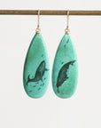 Teardrop-shaped earrings with whale design on a white background