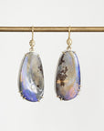 A pair of gold drop earrings with teardrop-shaped iridescent opal gemstones, hanging from a gold rod against a light gray background.
