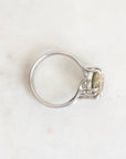 A silver ring with a small oval yellow-green gemstone in a prong setting, photographed on a light marble surface.