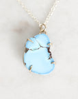 A light blue turquoise stone pendant necklace with gold wire wrapping and a silver chain, displayed on a light marble surface.