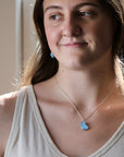 A woman wearing a silver chain necklace with a light blue elephant pendant, paired with a beige tank top.