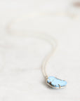 A delicate silver necklace with a light blue stone pendant, resting on a light marble surface.