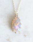 Purple and pink opal pendant set in yellow gold prongs against a marble background.