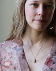 Woman wearing opal necklace and floral blouse smiling at the camera against an indoor background.