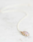 Opal necklace with silver chain and gold prongs laying on a marble background.