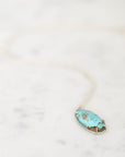 A silver necklace with an oval turquoise pendant resting on a light marble surface.