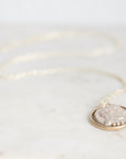A silver-toned coin pendant necklace with a gold-toned bezel, resting on a light marble surface.