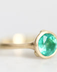 Gold bezel set ring with bright emerald green gemstone turned to the side against a white background.